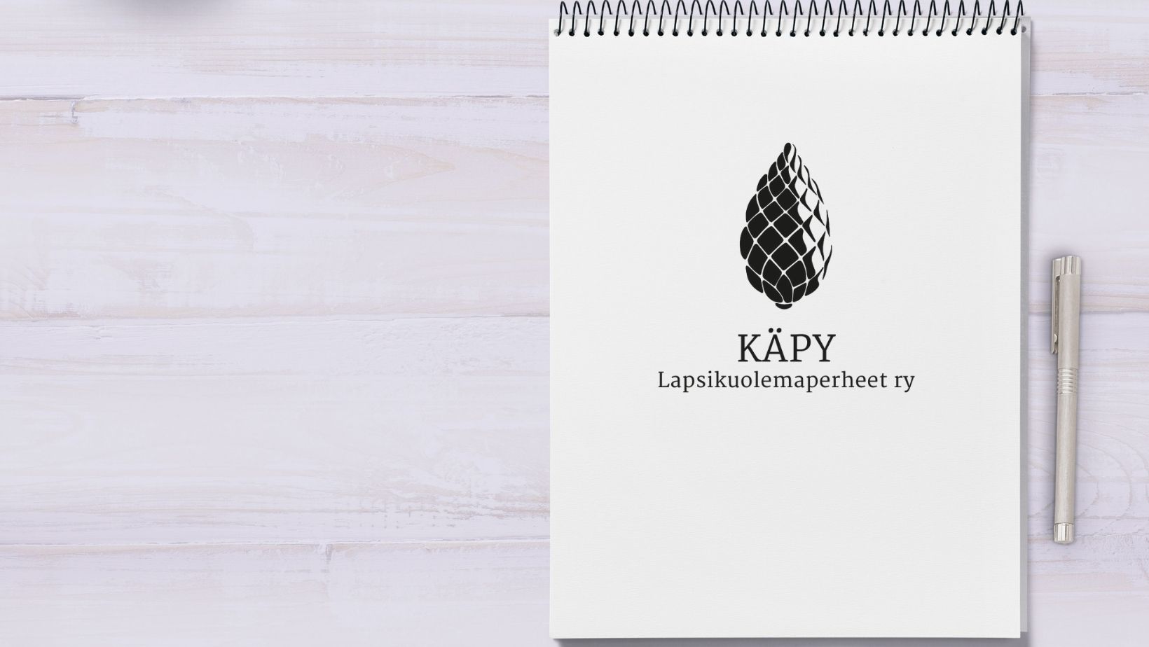 Käpy ry:n logo muistilehtiön päällä, vieressä kynä