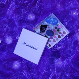 Muistokivet laatikossa kansi avoinna vieressä, kivien alla laatikossa näkyy tarra-arkki ja vihko